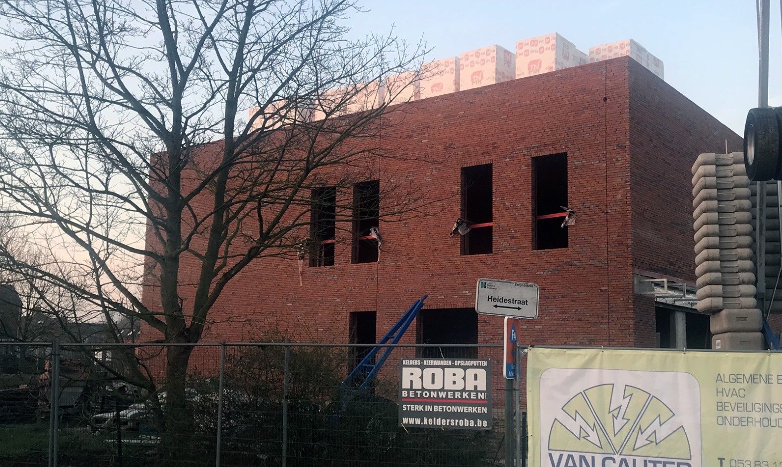 Nieuwbouw in rode baksteen met het werfdoek van Van Cauter aan de omheining